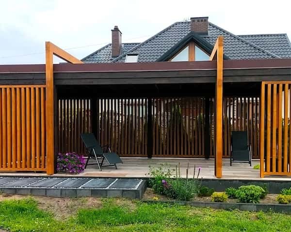 Ażurowa drewniana pergola zadaszająca taras, utrzymana w sp&oacute;jnym stylu z wiatą i konstrukcją domu.