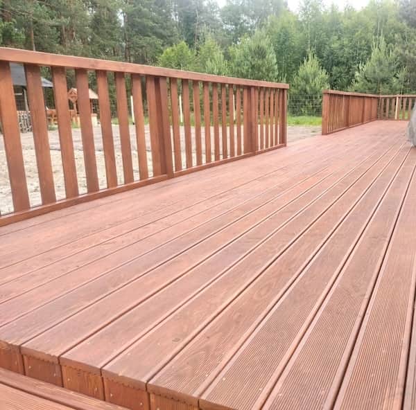 Przestronny taras z naturalnego drewna stanowiący płynne przejście między domem szkieletowym a ogrodem.